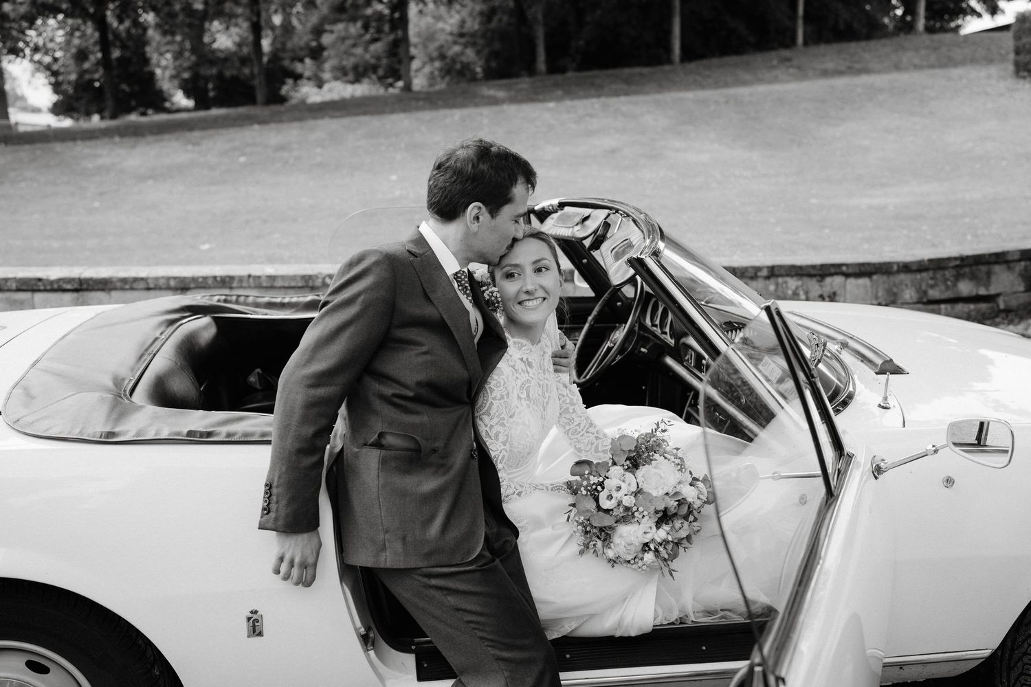 Wedding couple waves from vintage white car during departure.