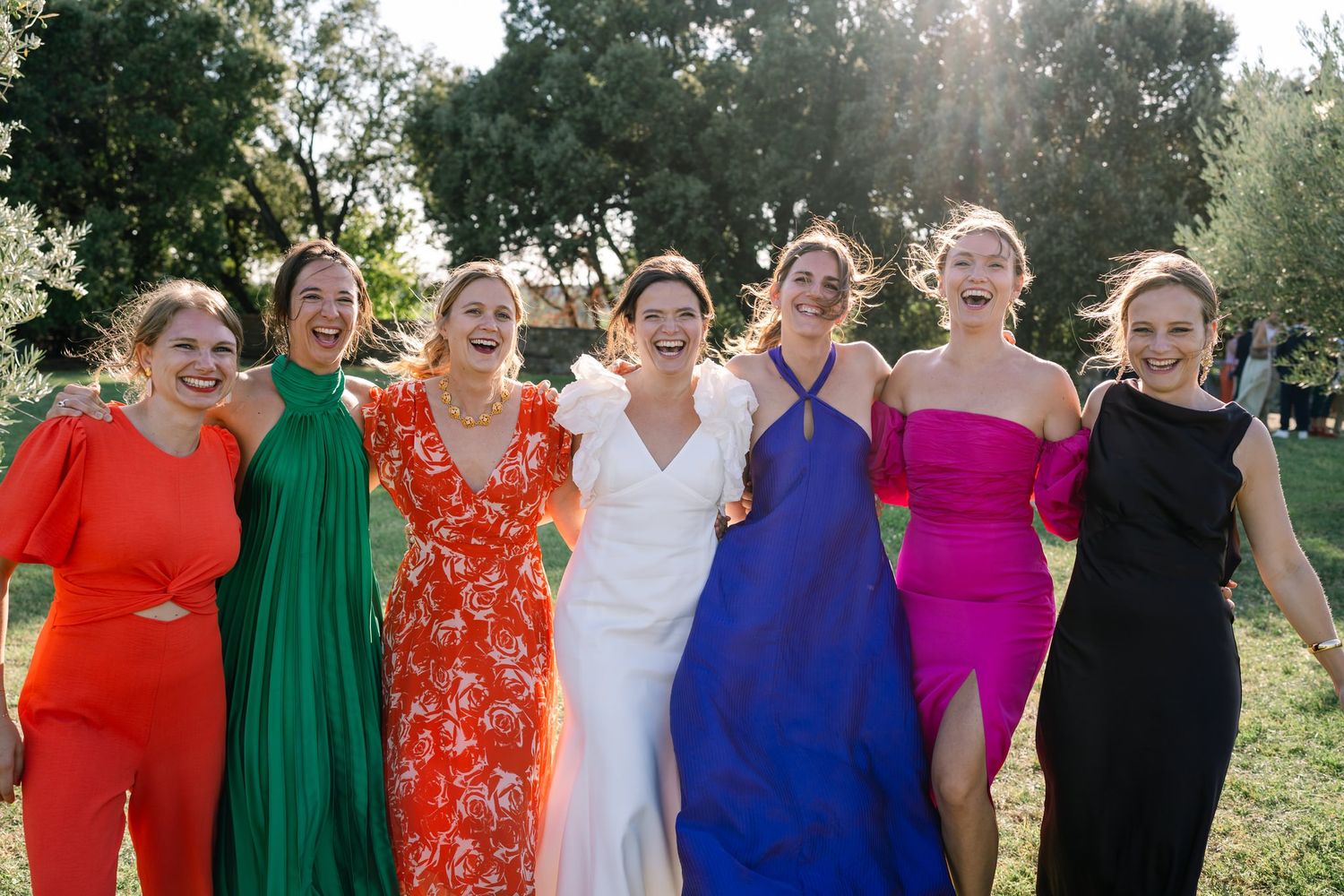 Wedding party wearing vibrant rainbow-colored dresses posing together outdoors.