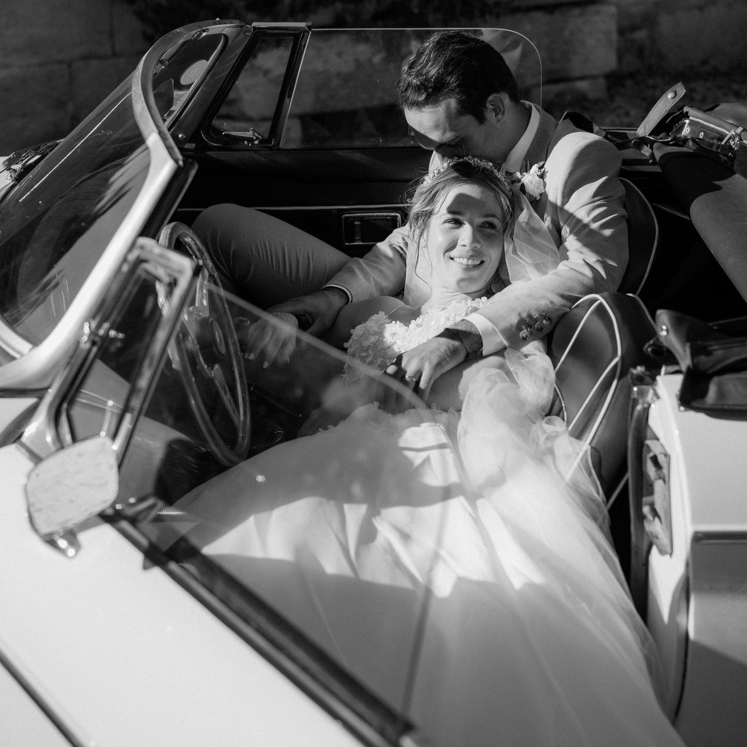 Black and white photo of couple riding in vintage convertible car.