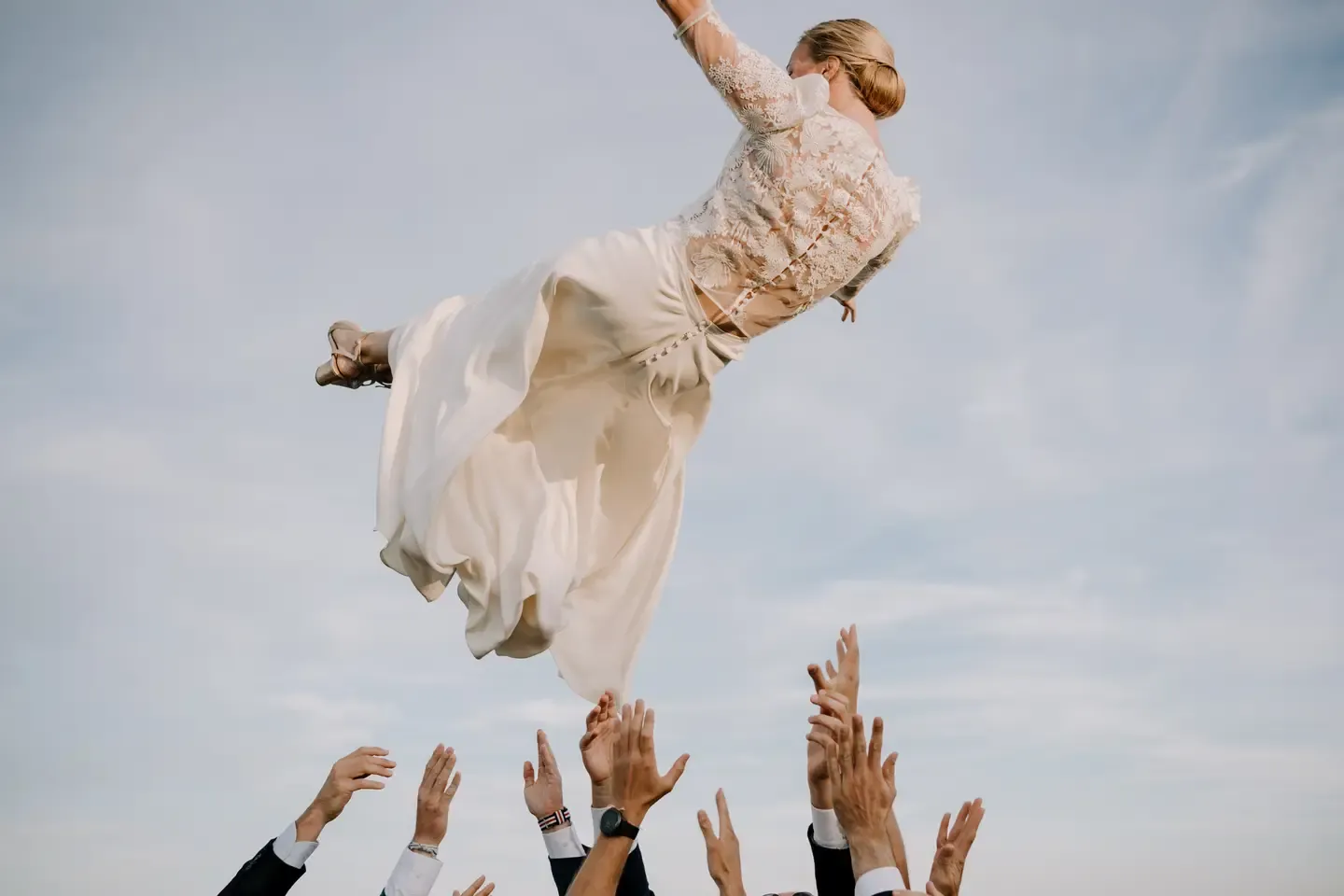 Wedding guests toss a bride and groom into the air during a celebratory moment.