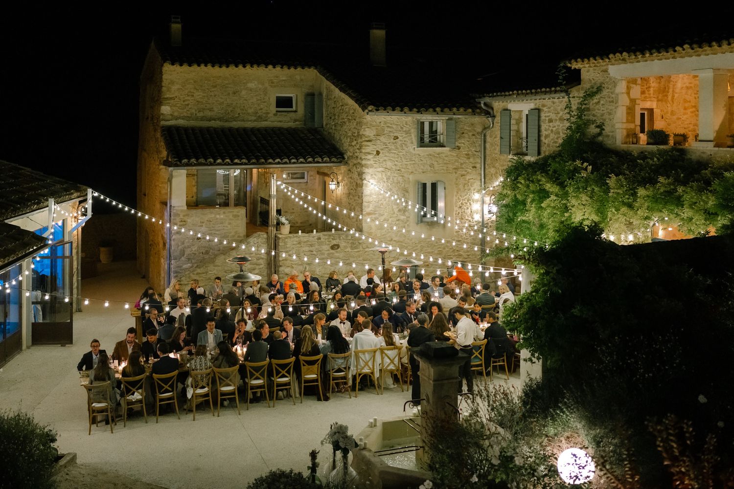 Aerial view of an outdoor wedding reception venue lit by string lights at night.