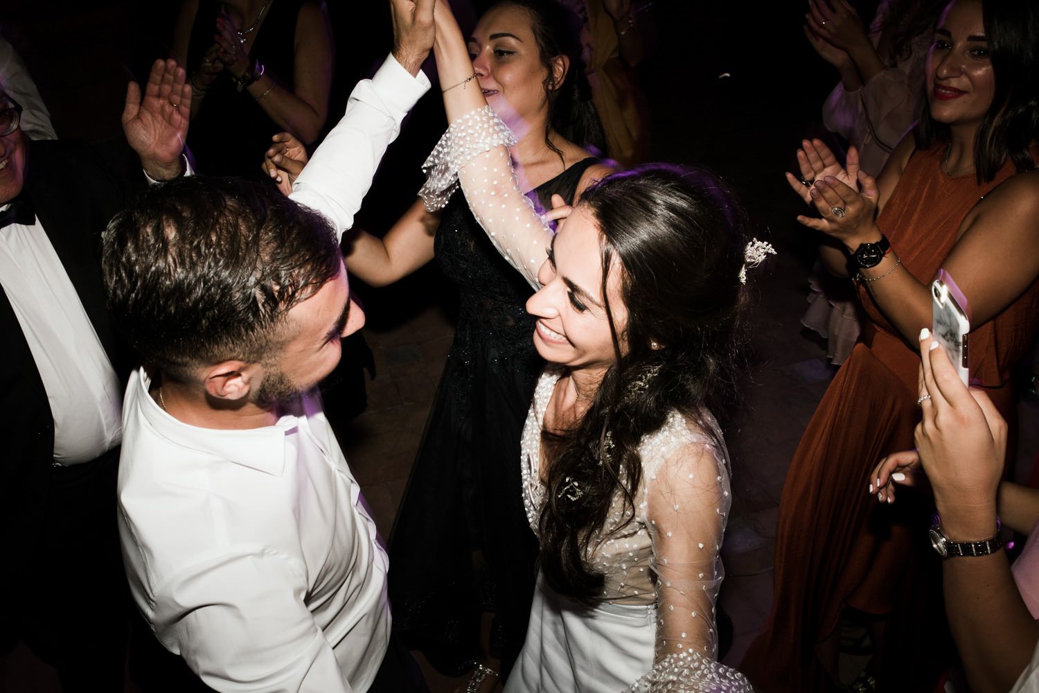 Wedding guests dancing and celebrating on a dark dance floor at a reception party.