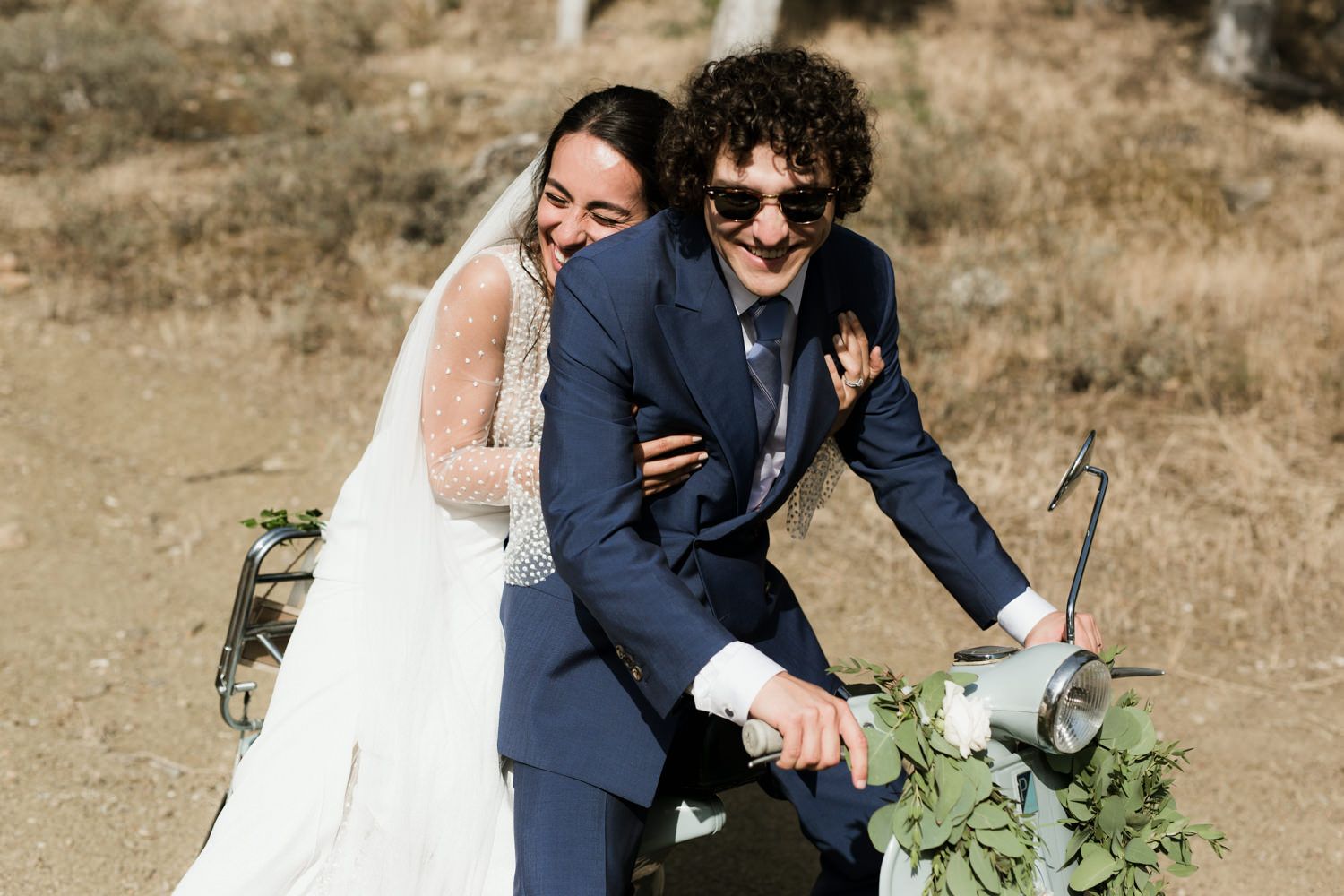 Wedding couple sharing joyful moment on vintage scooter in rustic setting.