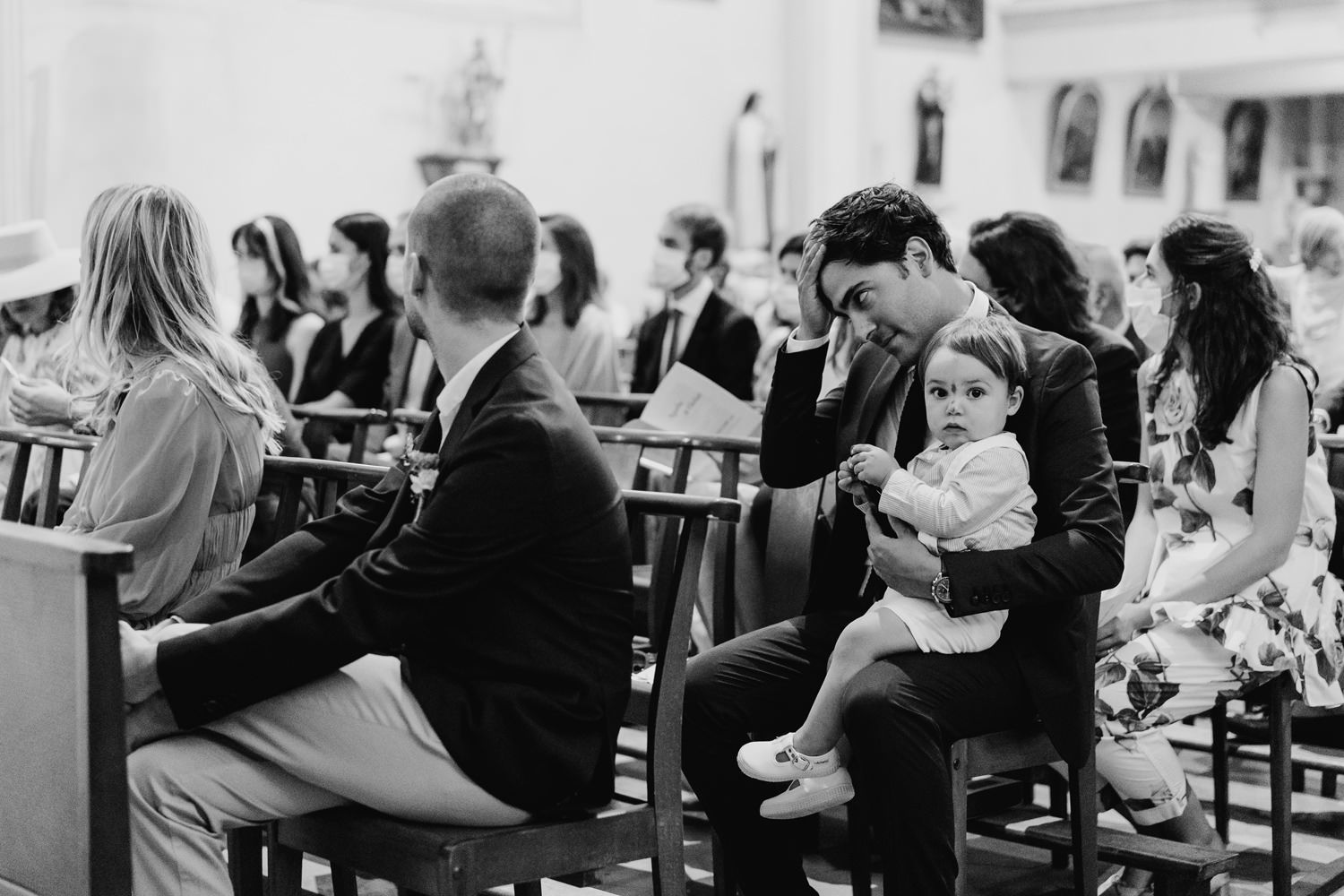 Wedding guests seated in church pews during a ceremony with a small child.