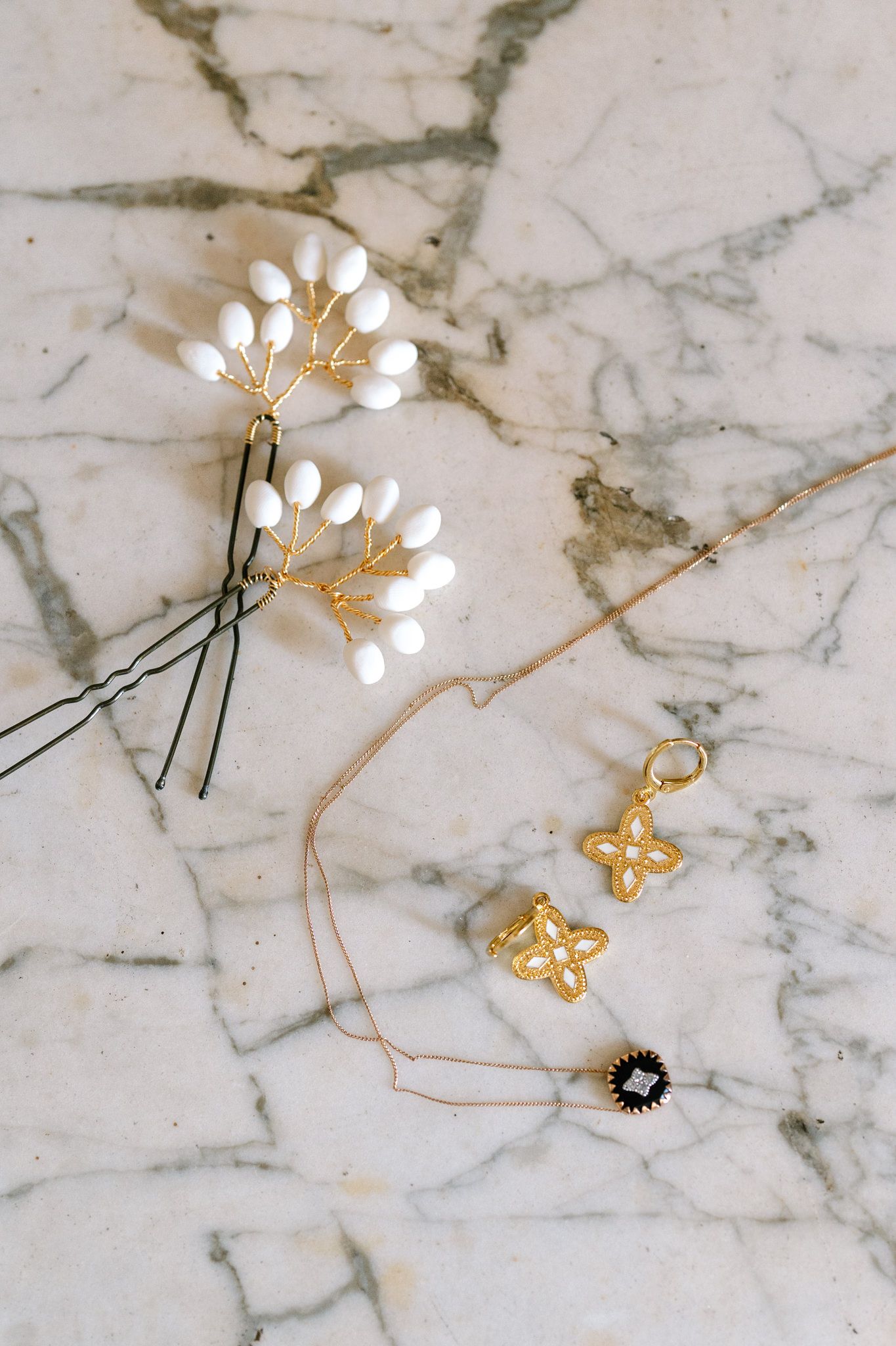Delicate gold and pearl hair accessories arranged on white marble surface.