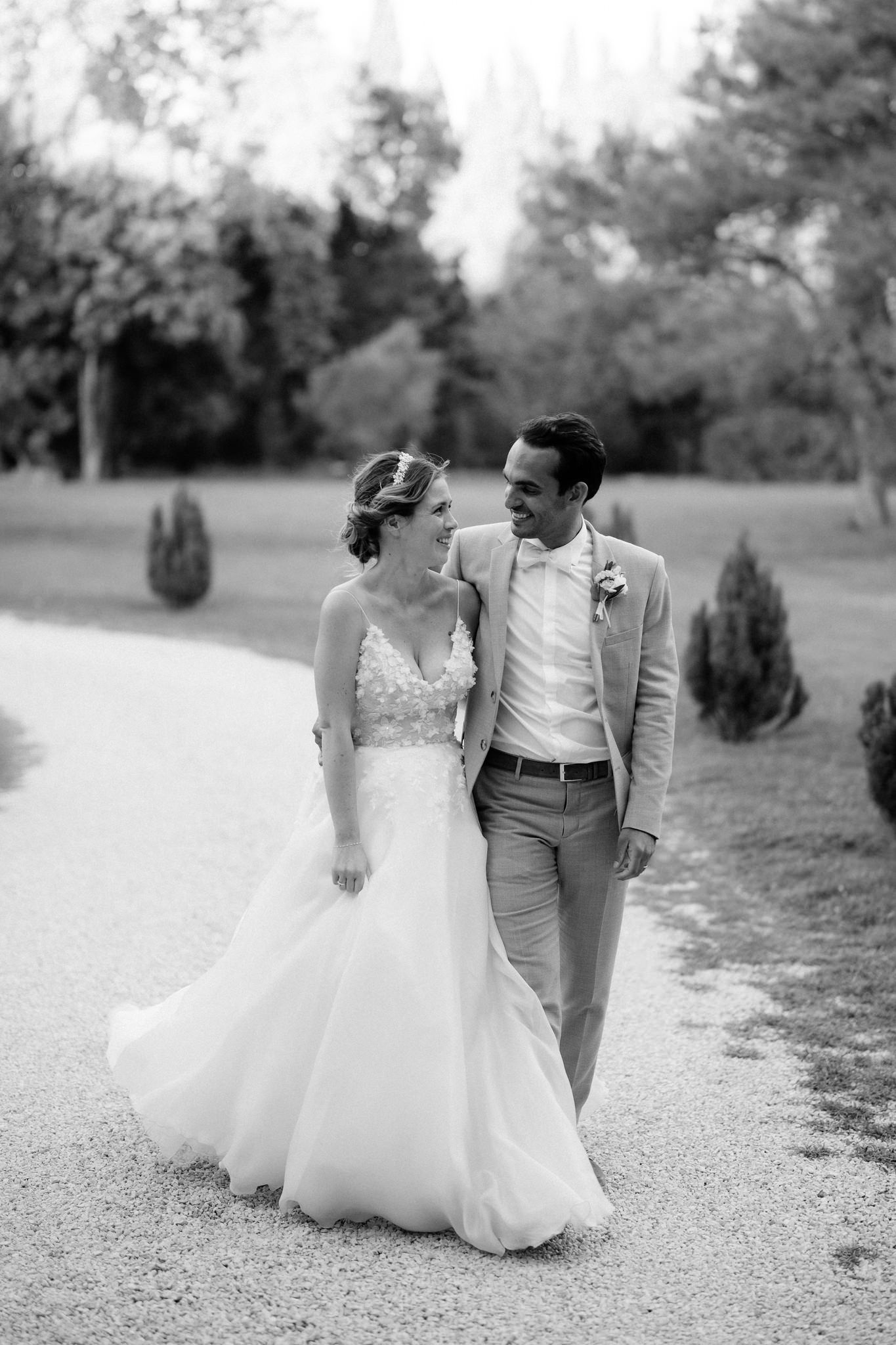 A romantic black and white photo of a couple walking along a tree-lined path.