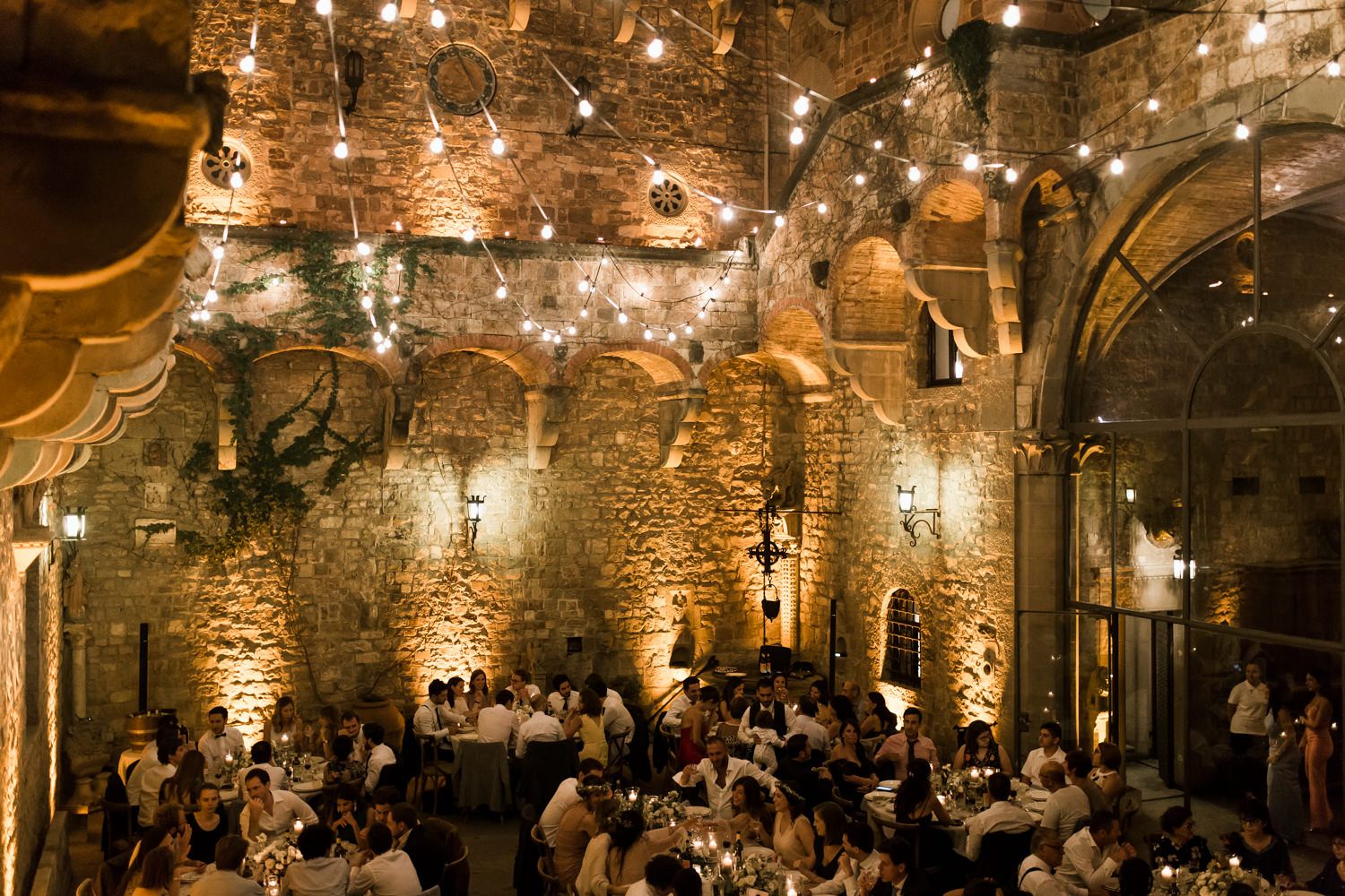 Romantic evening wedding reception in stone castle hall with warm lighting.