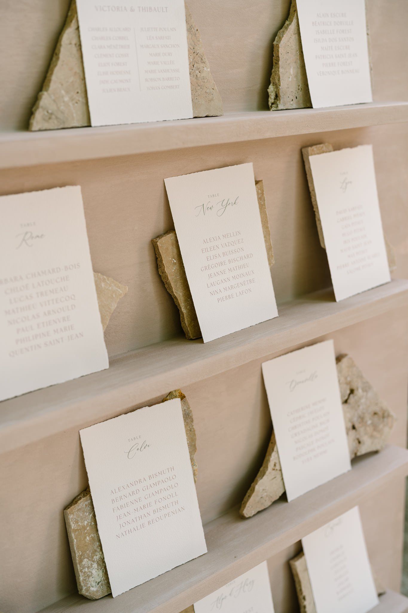 Wedding seating chart display with white cards arranged on beige wall.