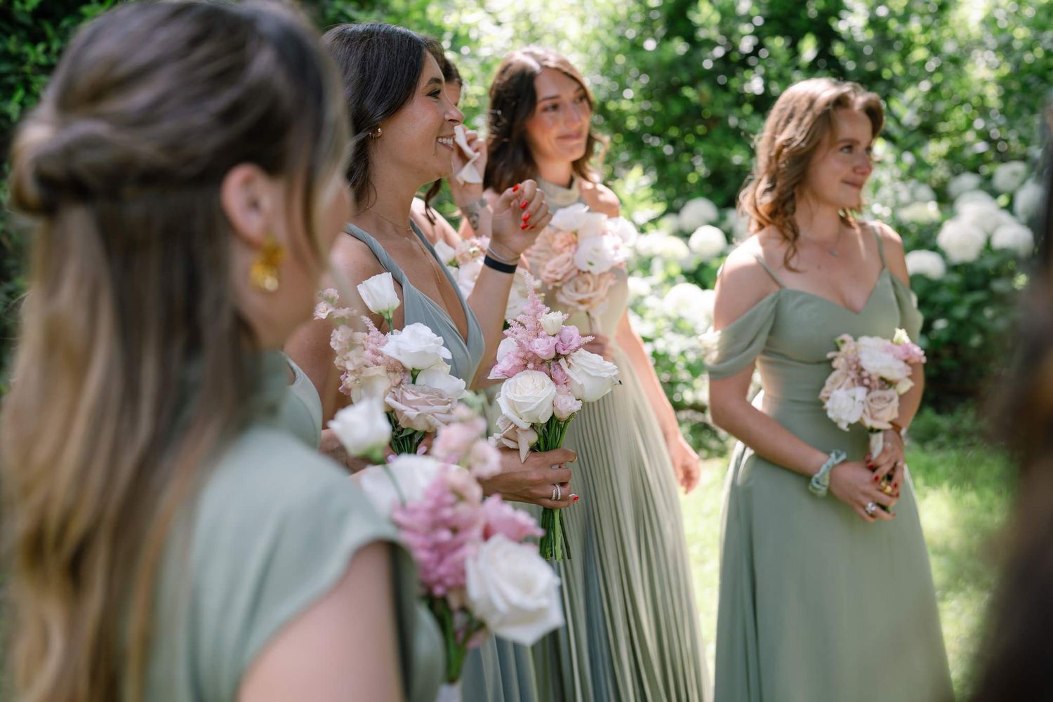 Candid photo of bridesmaids in sage green dresses holding pink and white bouquets.