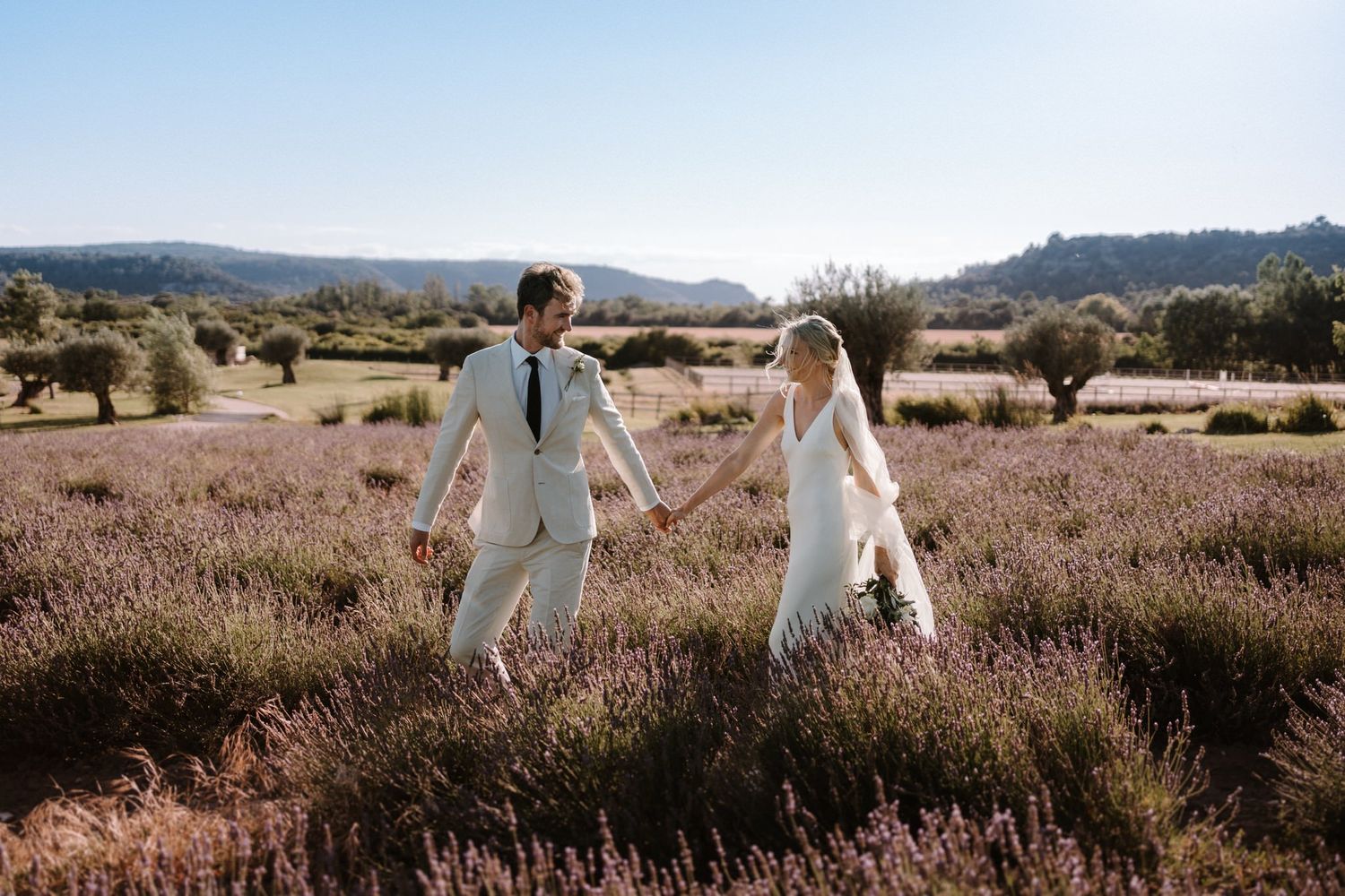 Two people stroll hand in hand through a desert landscape at sunset.