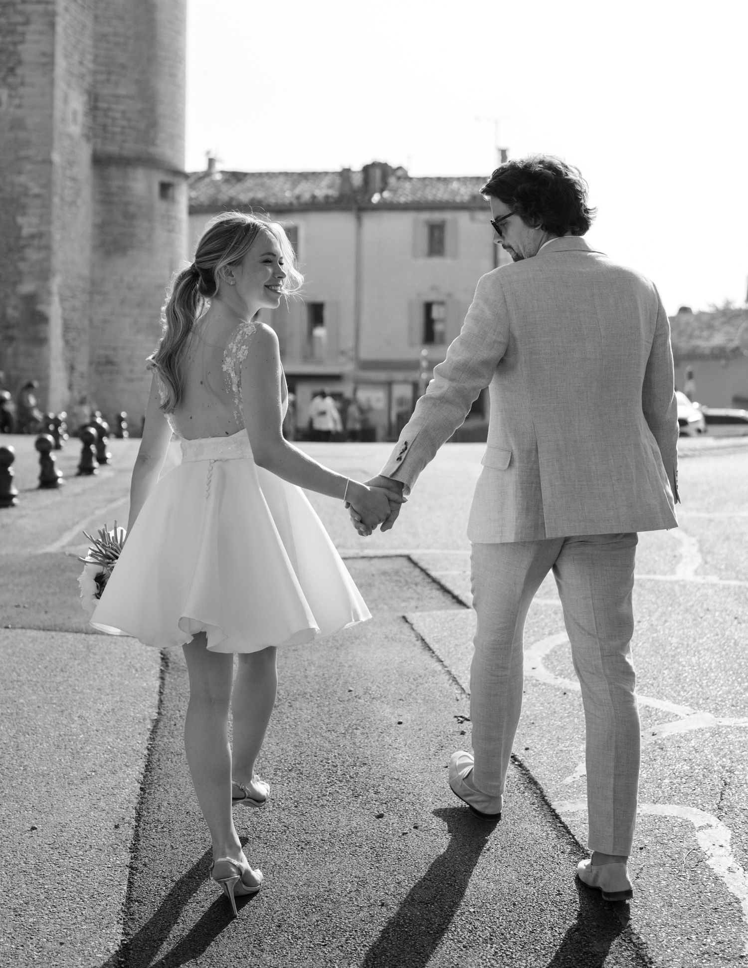 Black and white photo of couple dancing playfully on stone pavement.