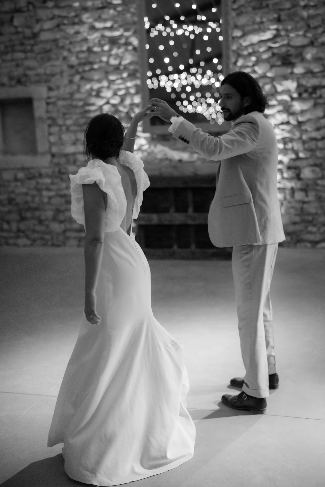 First dance at a wedding with twinkling lights overhead in a rustic stone venue.