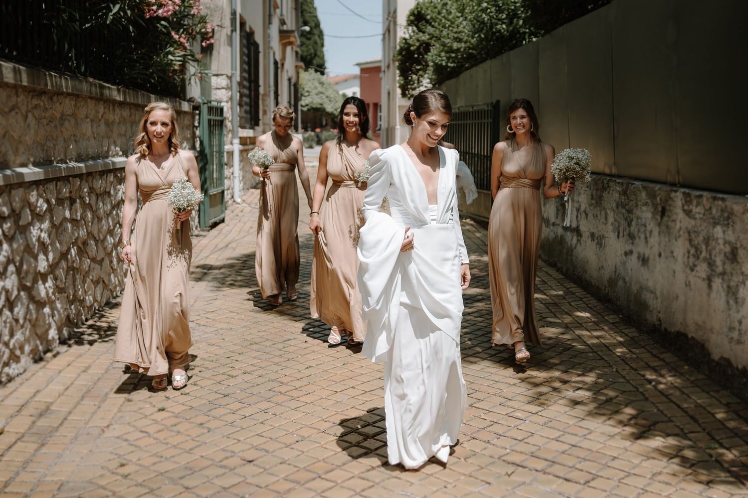 Wedding procession walking along stone pathway in neutral and white attire.