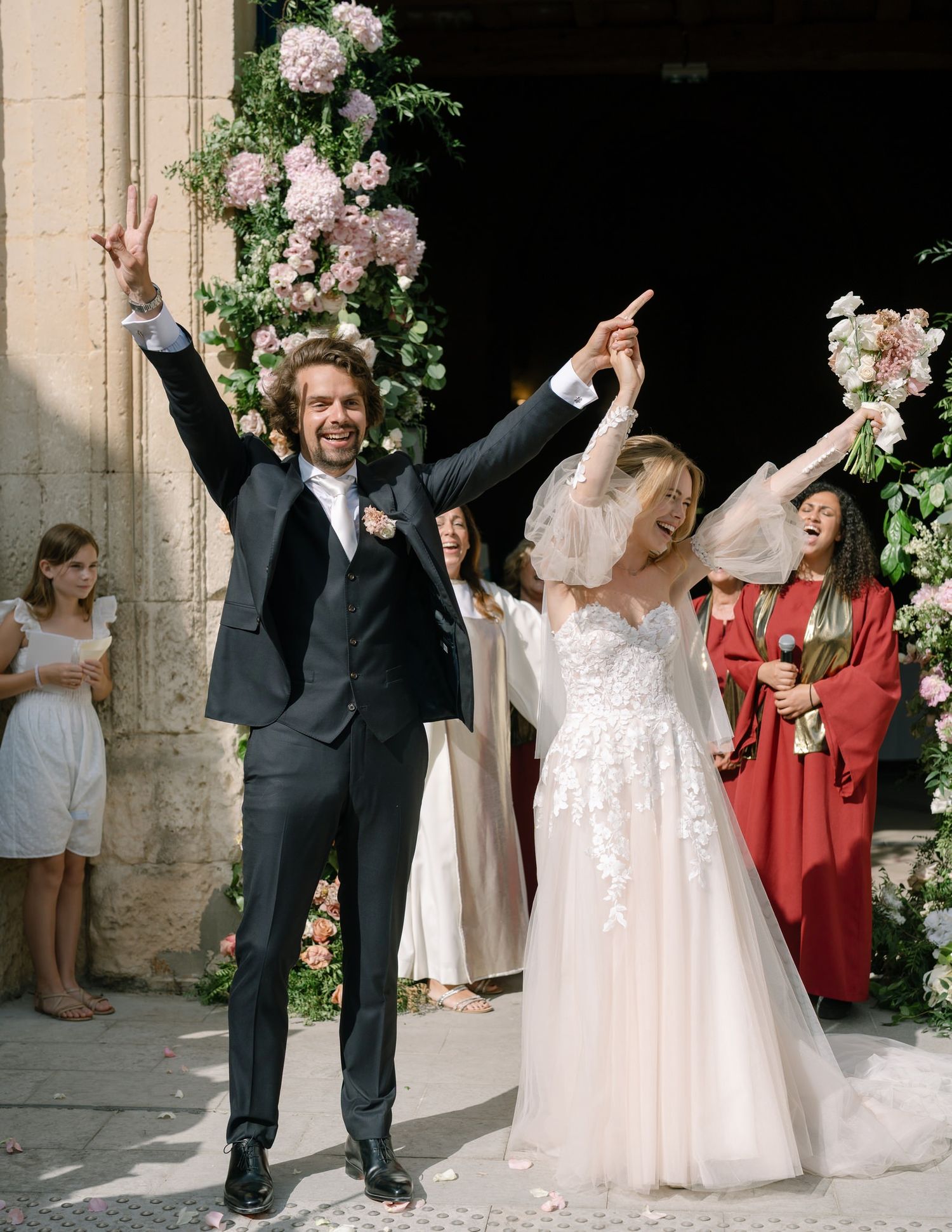 Wedding celebration outside stone church entrance decorated with pink and white floral arrangements.