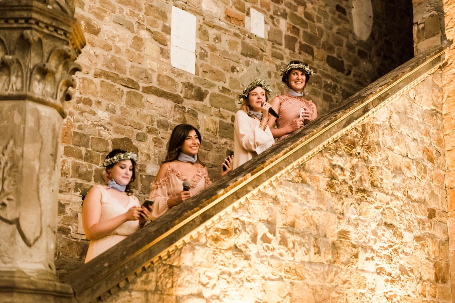 Wedding party poses on historic stone staircase in castle setting.