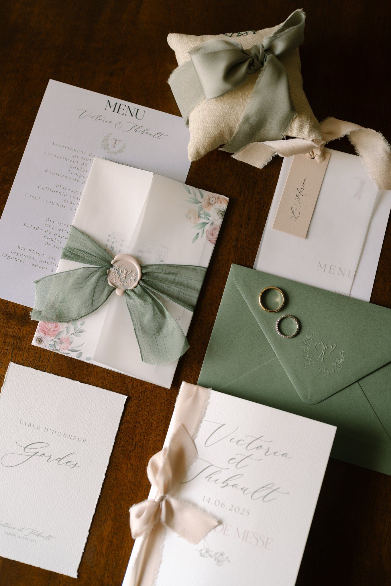 Elegant wedding invitations with sage green envelopes and white wax seals on wooden surface.