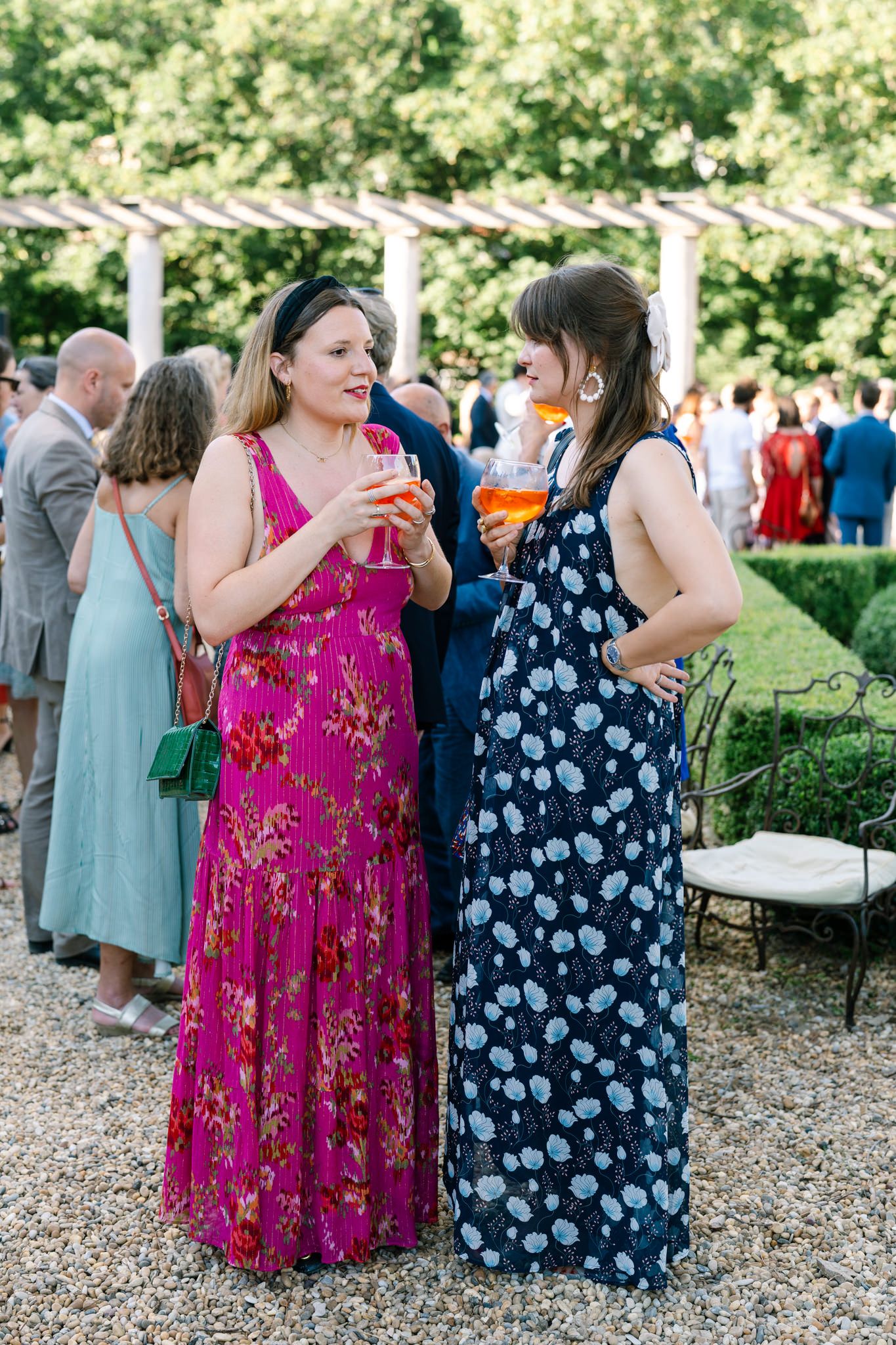 Wedding guests in colorful summer dresses mingle during an outdoor reception.