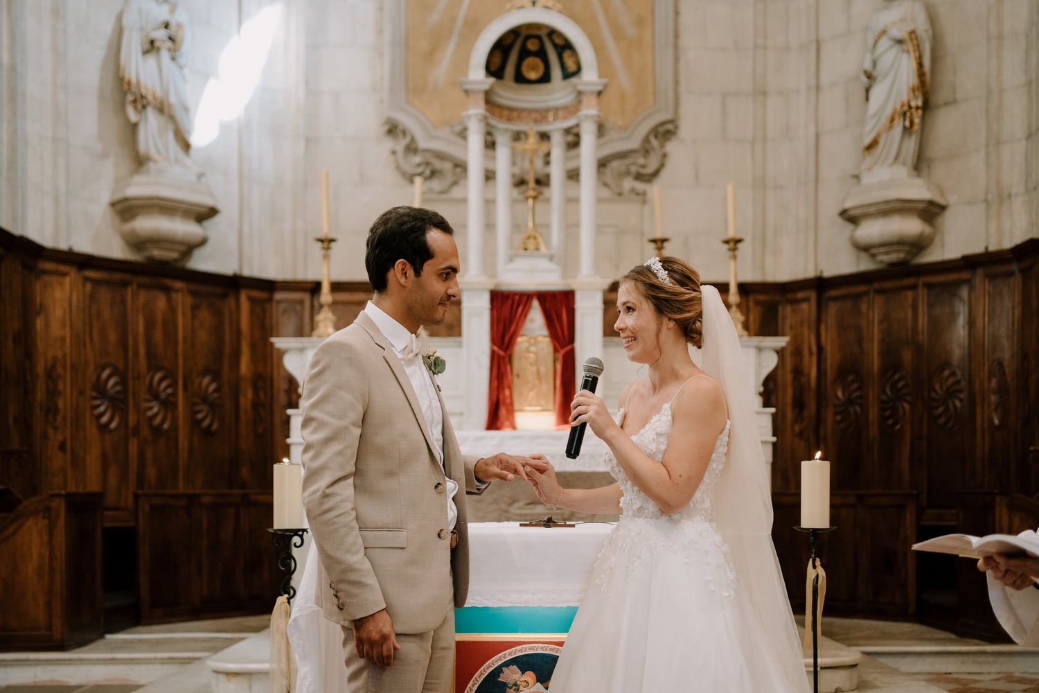 Wedding ceremony proceedings in a traditional stone church with religious artwork.