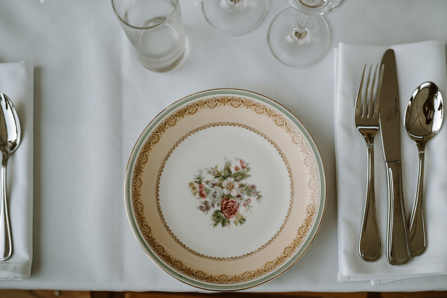 Elegant place settings with vintage floral plates and silverware arranged on white tablecloths.
