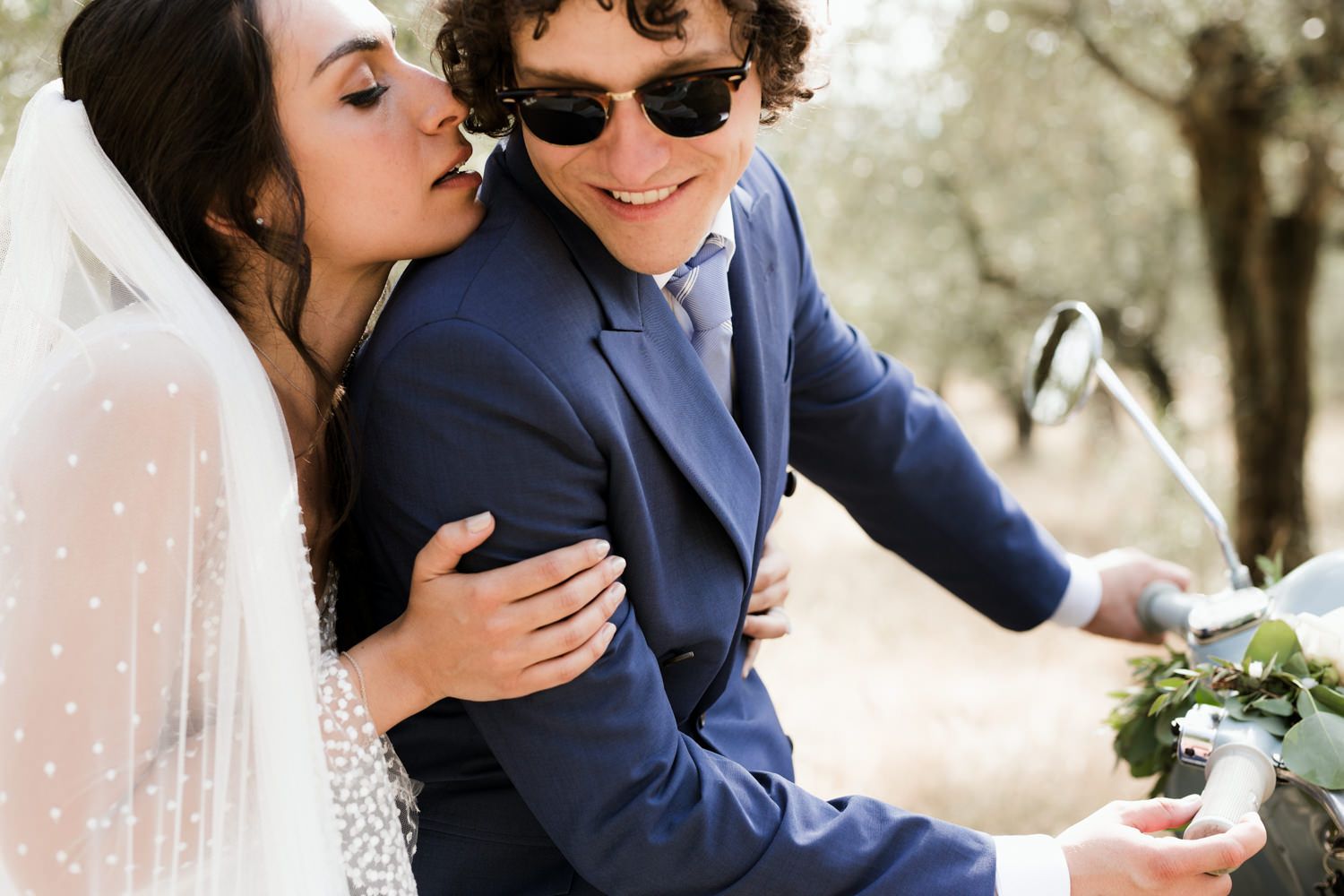Romantic moment shared on vintage Vespa scooter during wedding photoshoot.