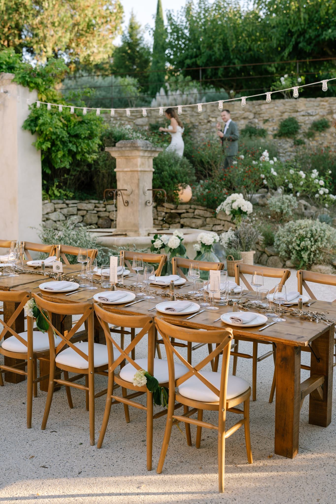An elegant outdoor wedding reception table setup with wooden chairs and string lights.