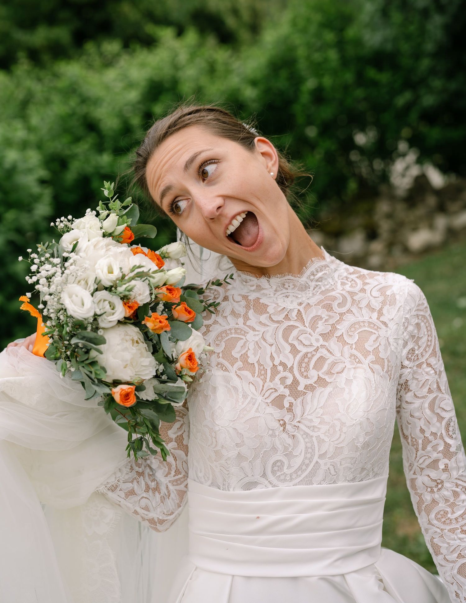 Elegant white lace wedding dress with floral bouquet details shown in garden setting.