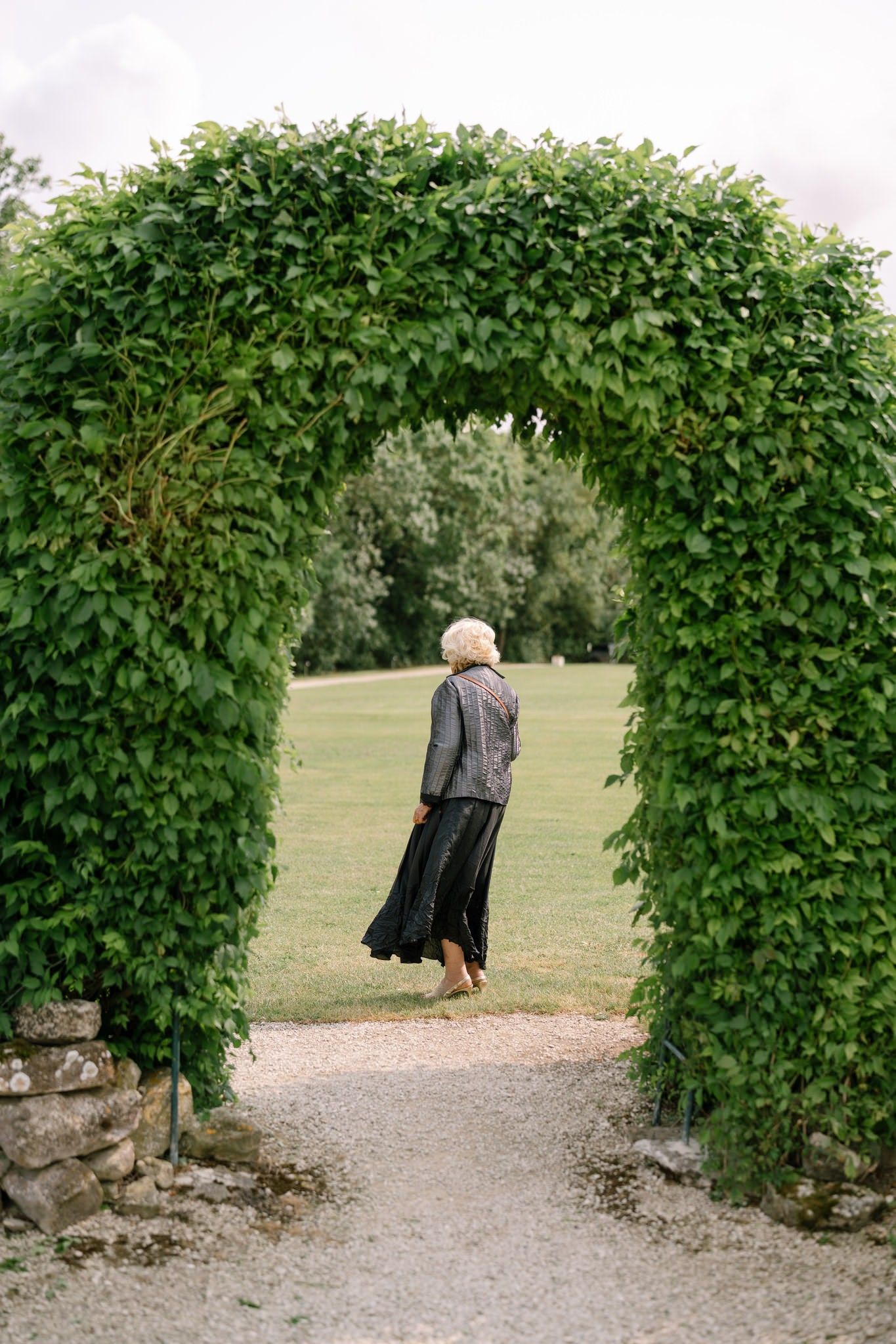 Stone path leading through a lush green archway in a garden setting.