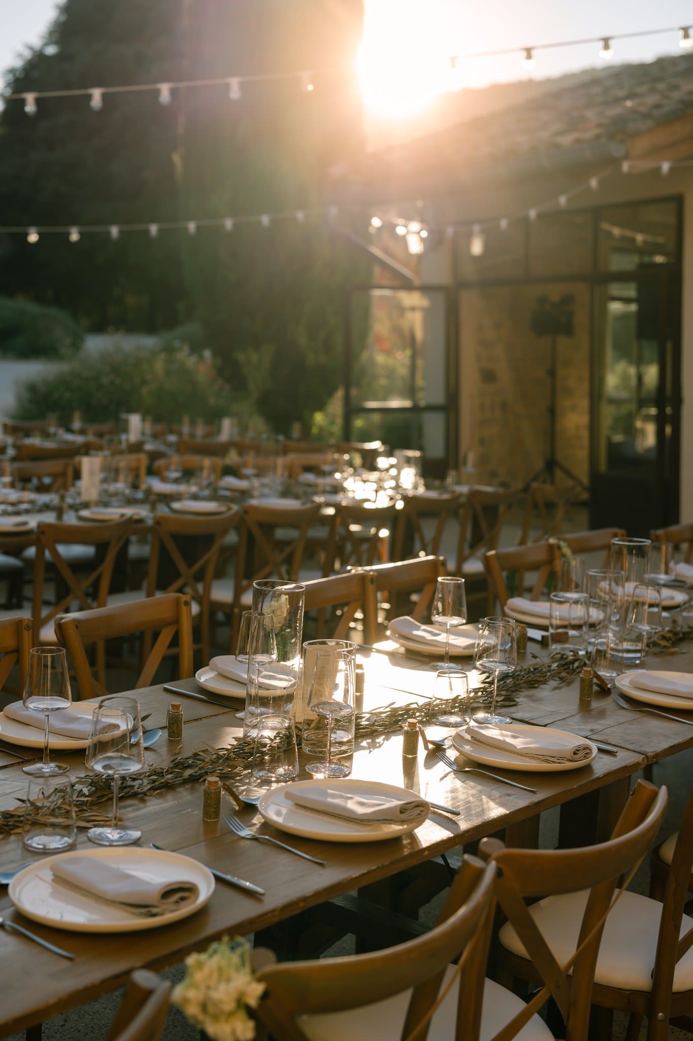 Wedding reception tables set with elegant place settings under string lights at dusk.
