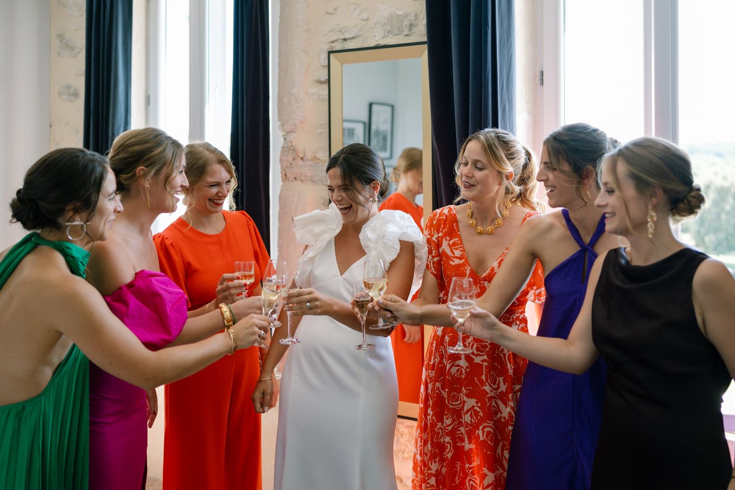 Wedding party in colorful dresses celebrating together in a bright indoor space.