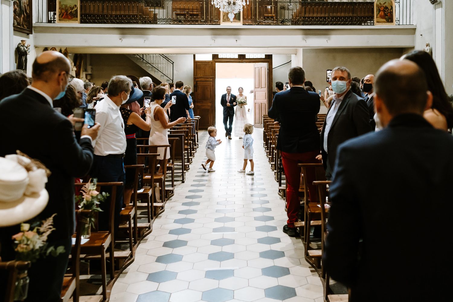Church aisle with checkered floor and wooden pews lined with guests.