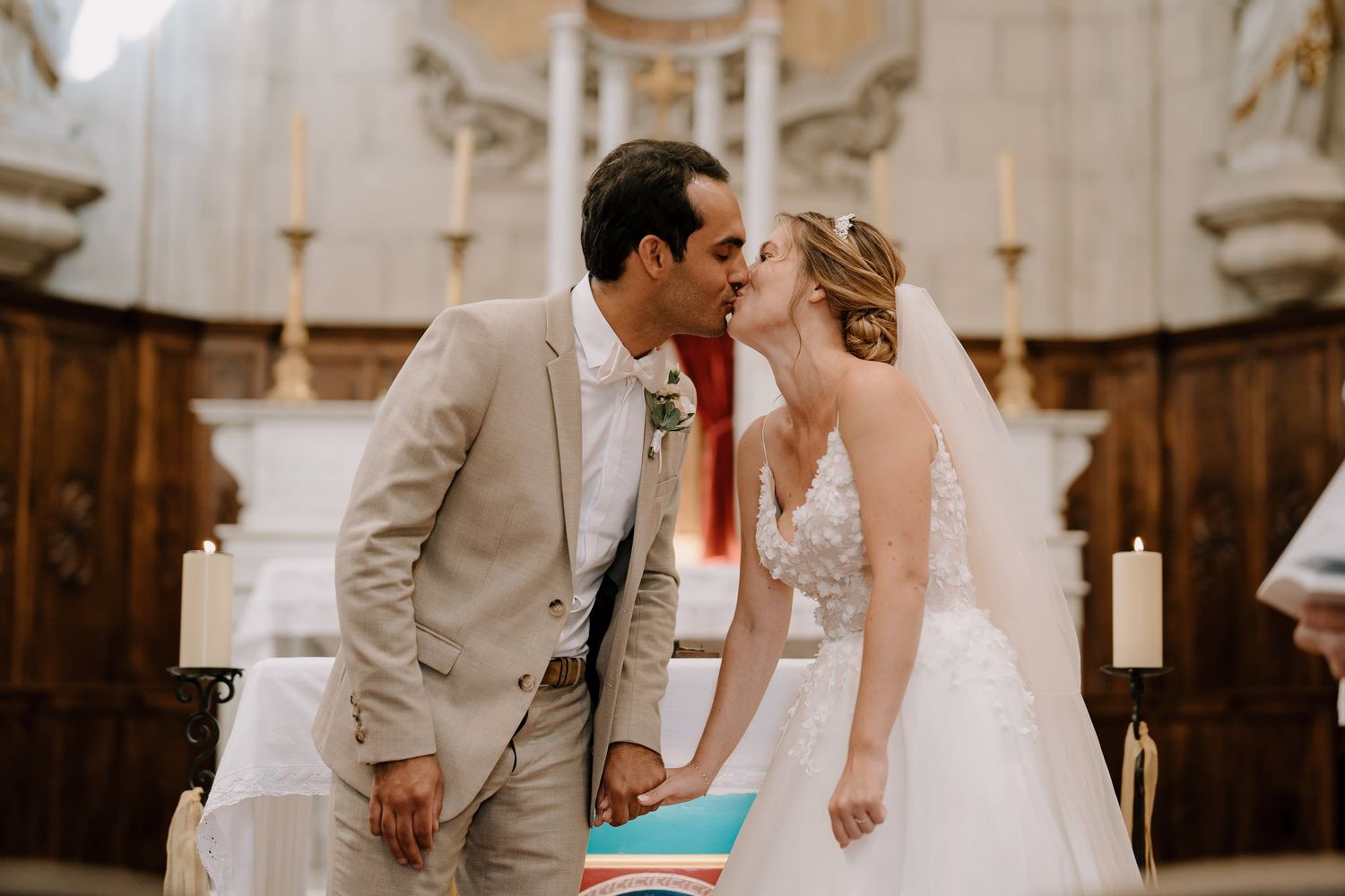 A romantic wedding ceremony kiss in a beautiful church with ornate architecture and candlelight.