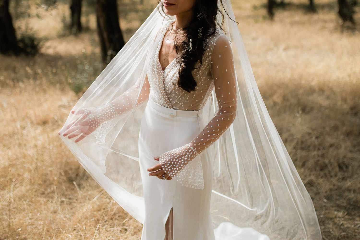 Elegant lace wedding dress with flowing veil captured in golden sunlight.