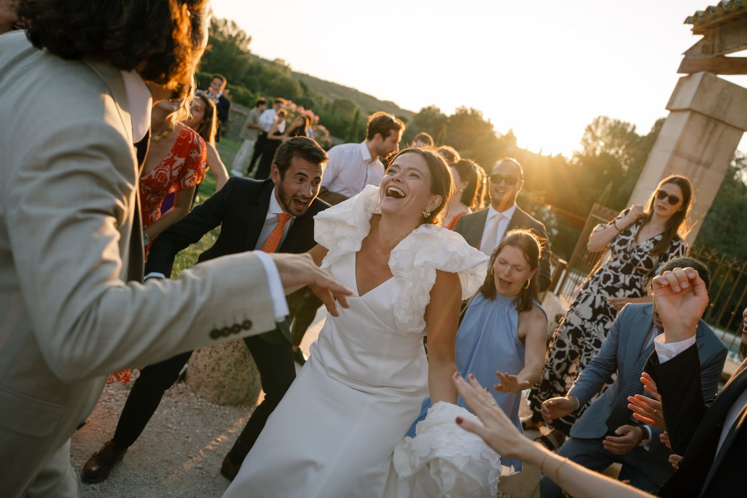 Wedding party celebrates outdoors during golden hour with guests dancing.