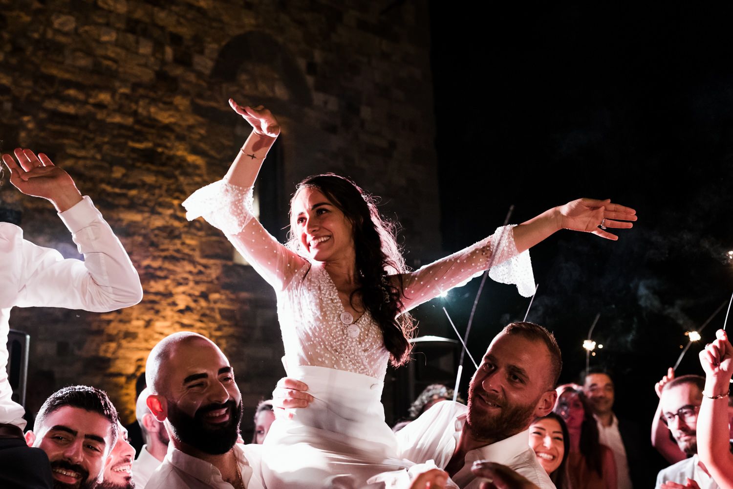 Wedding guests dance energetically on a dark dance floor with dramatic lighting at a reception celebration.