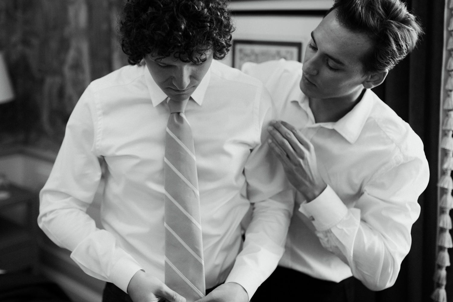 Two people in white dress shirts helping with formal attire preparations.