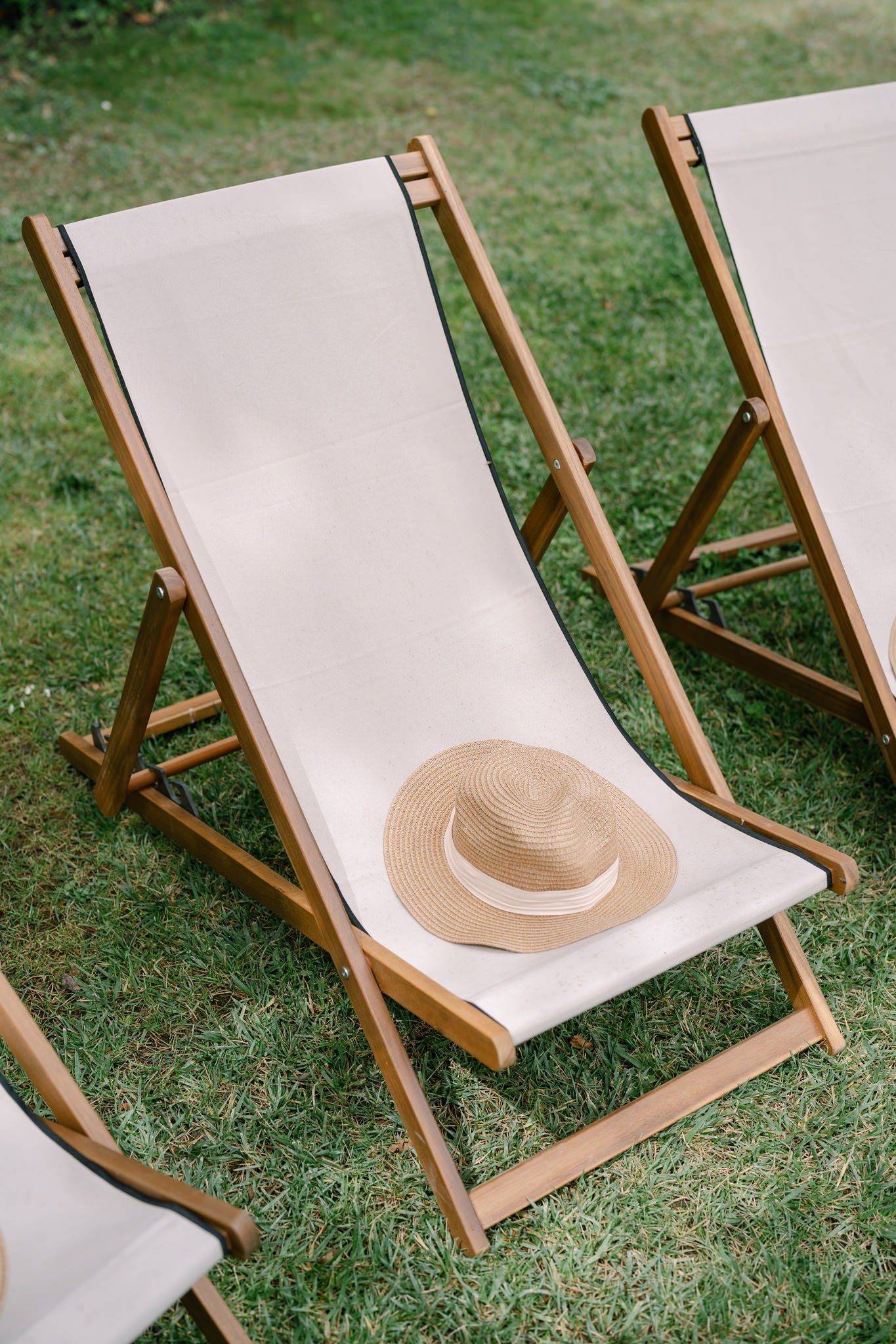 White canvas deck chairs set up on grass with a straw hat.
