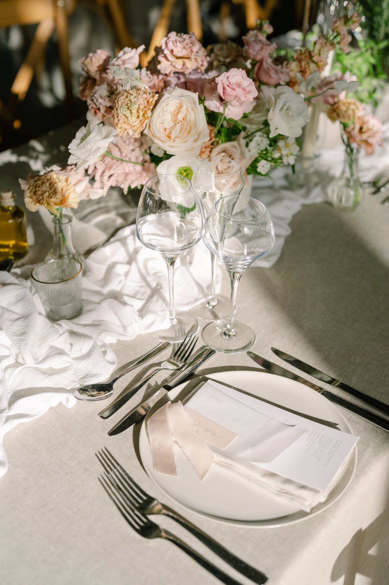 Close-up of formal place setting with white plates, silver cutlery and soft pink floral decorations.