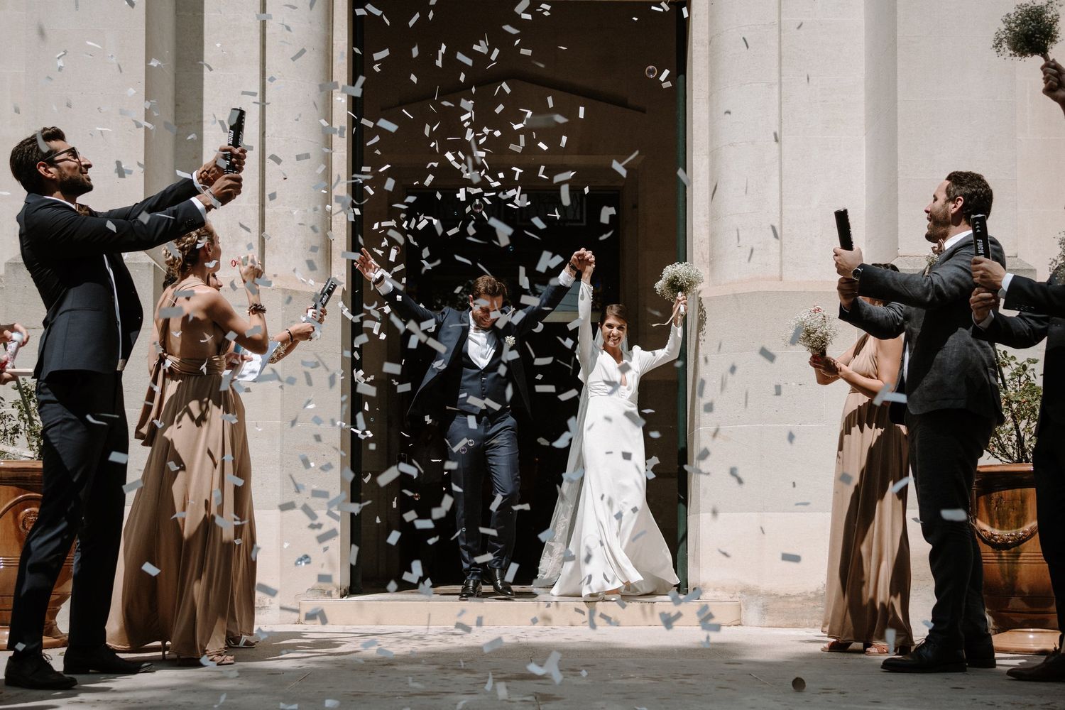 Confetti fills the air as wedding guests celebrate outside a white church building.