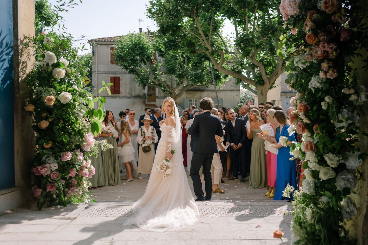 Wedding ceremony under a floral arch with guests watching the couple.