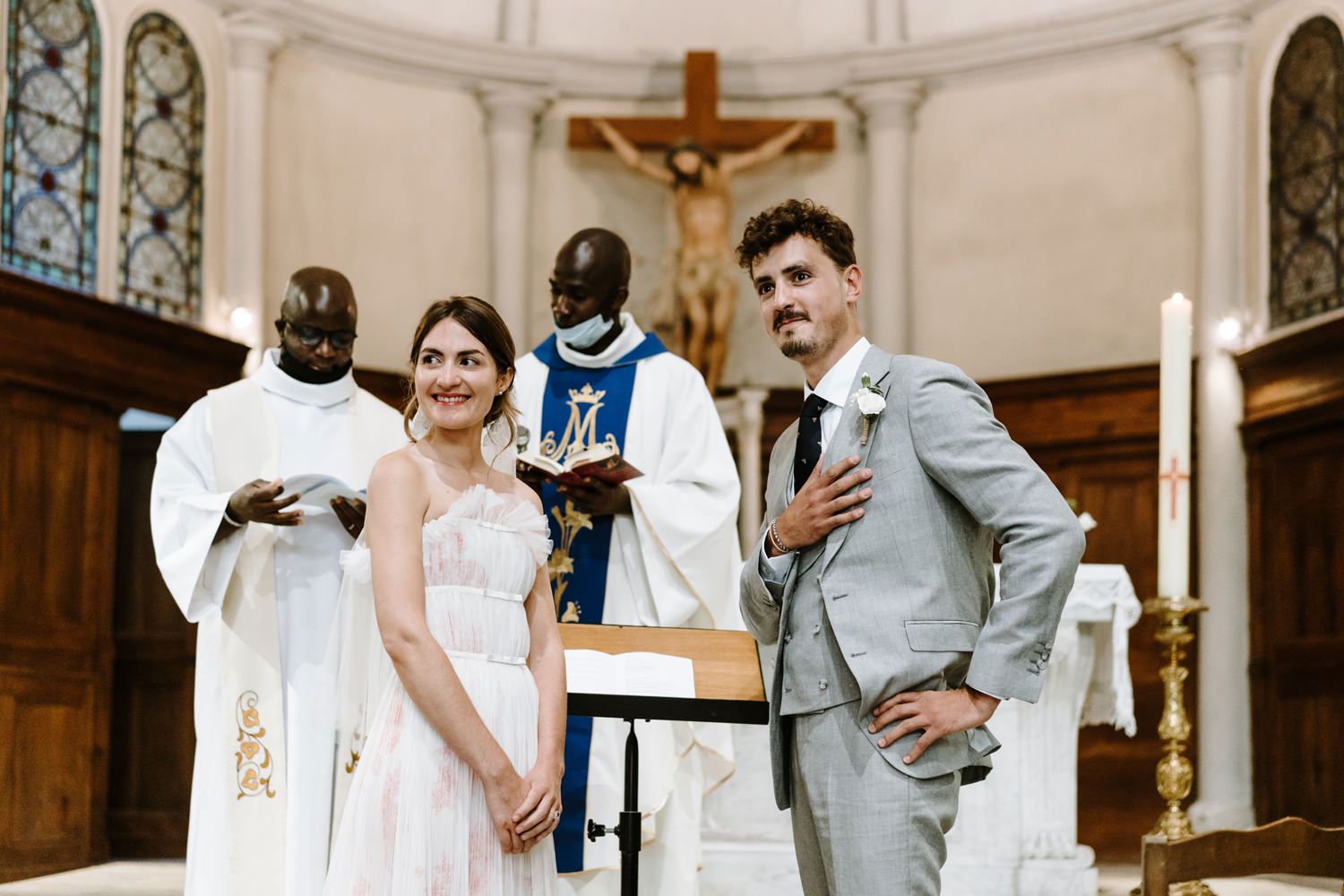 A wedding ceremony in progress inside a traditional church with stained glass windows and crucifix.
