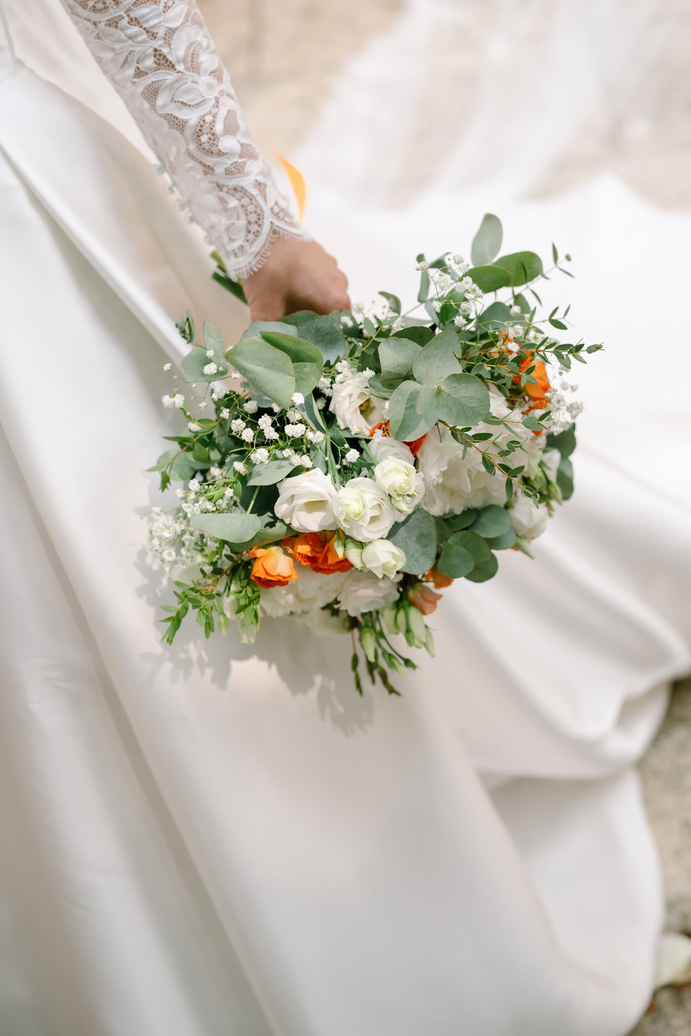 Close-up of white and orange floral bouquet details against wedding dress fabric.