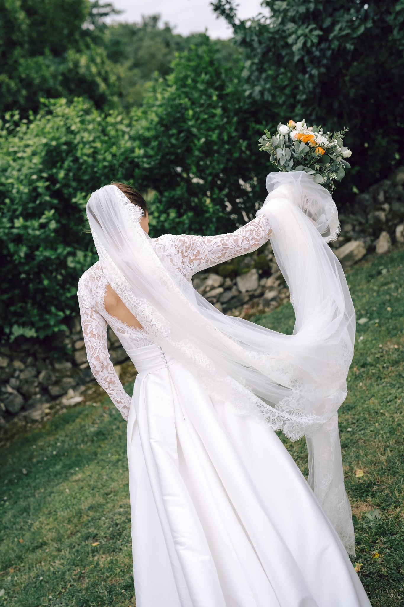 White lace wedding dress flowing in the wind against green garden background.