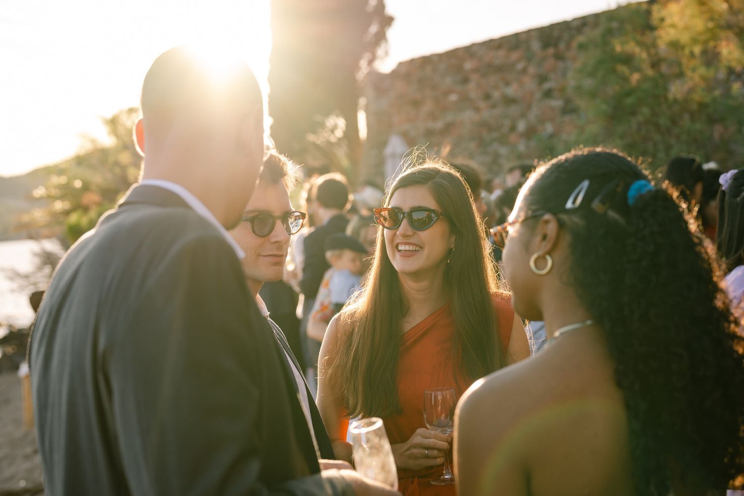 Wedding guests enjoying drinks at an outdoor sunset reception by the sea.