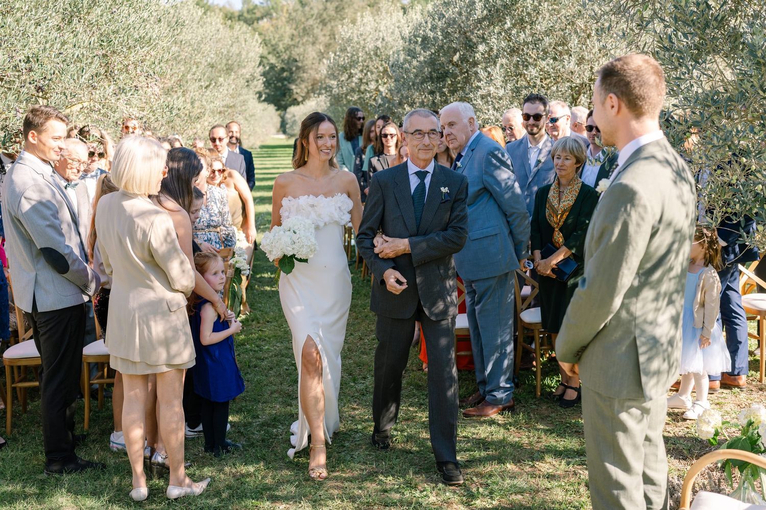 Wedding party and guests mingling in an outdoor orchard setting.