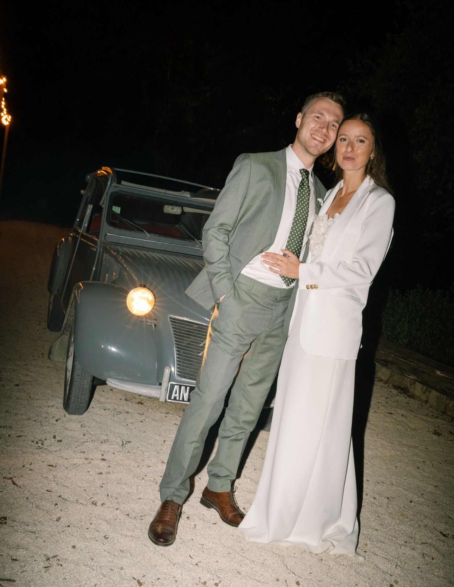 Candid nighttime photo of newlyweds standing beside their car.