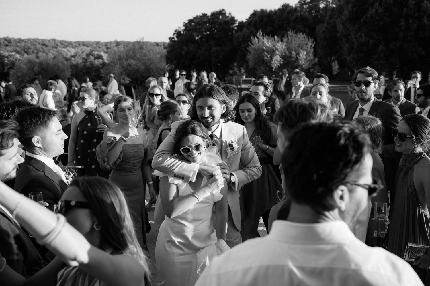 A joyful crowd of wedding guests dance together at an outdoor celebration.