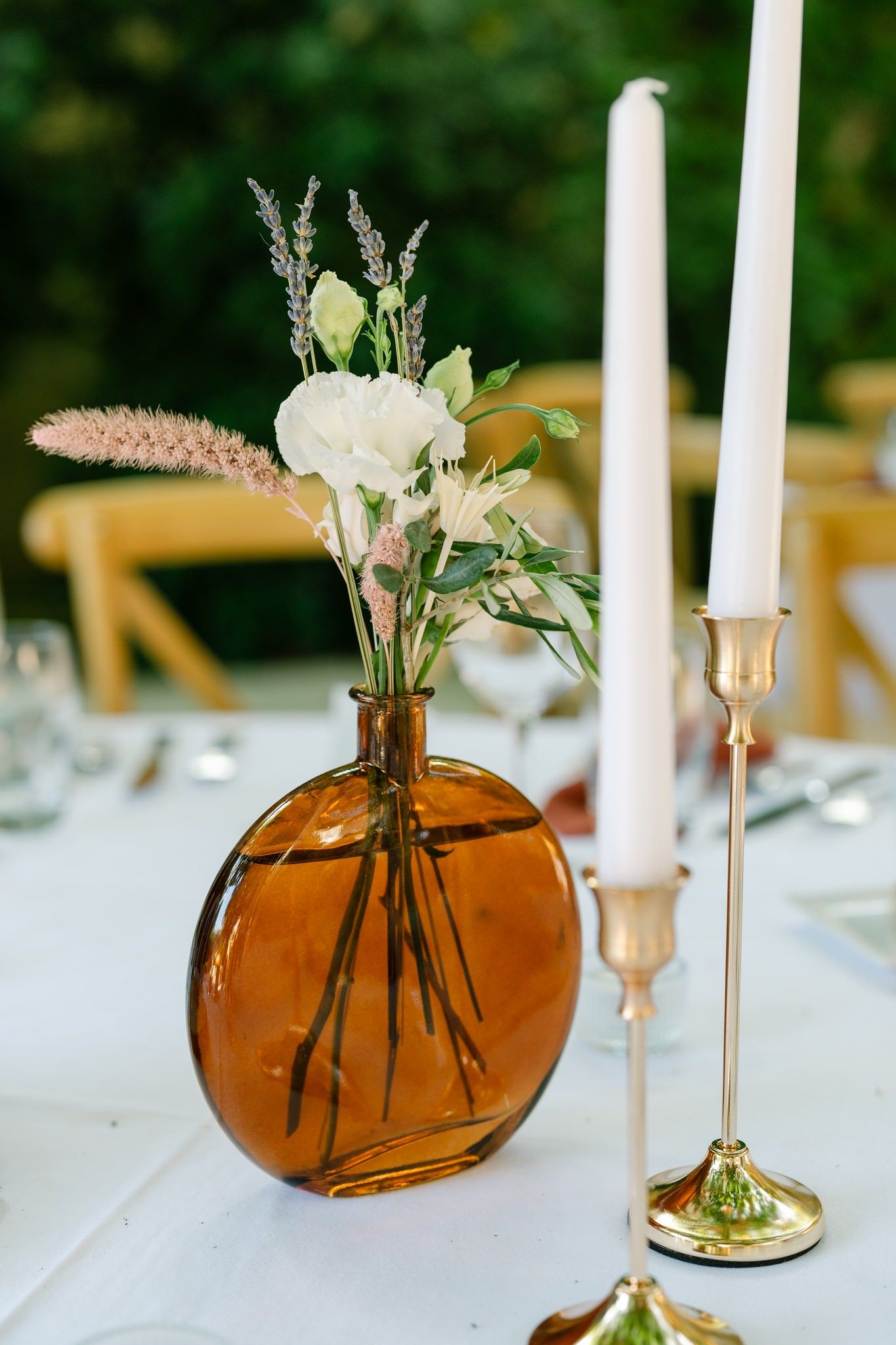 Amber glass vases with delicate floral arrangements and white candles create an elegant table setting.