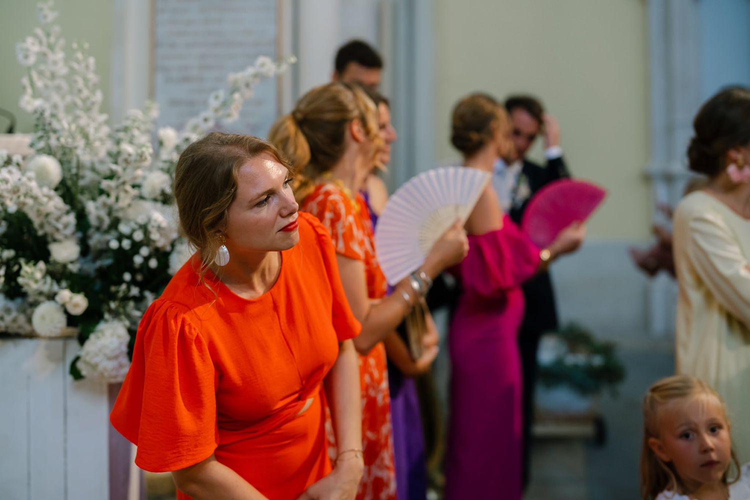 Wedding guests in vibrant orange and pink dresses during celebration.