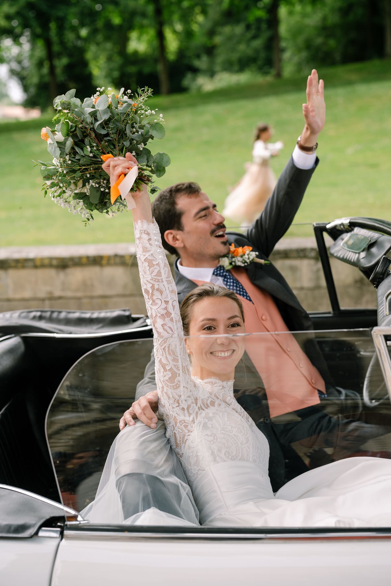 Newlyweds celebrate joyfully in classic white convertible car.