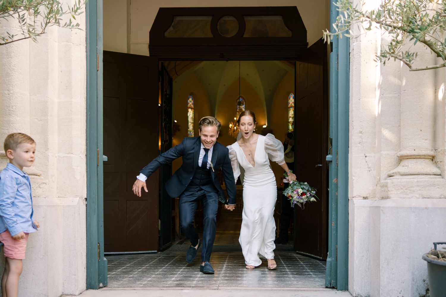 Wedding party gathered at church entrance with sunlight streaming through doorway.